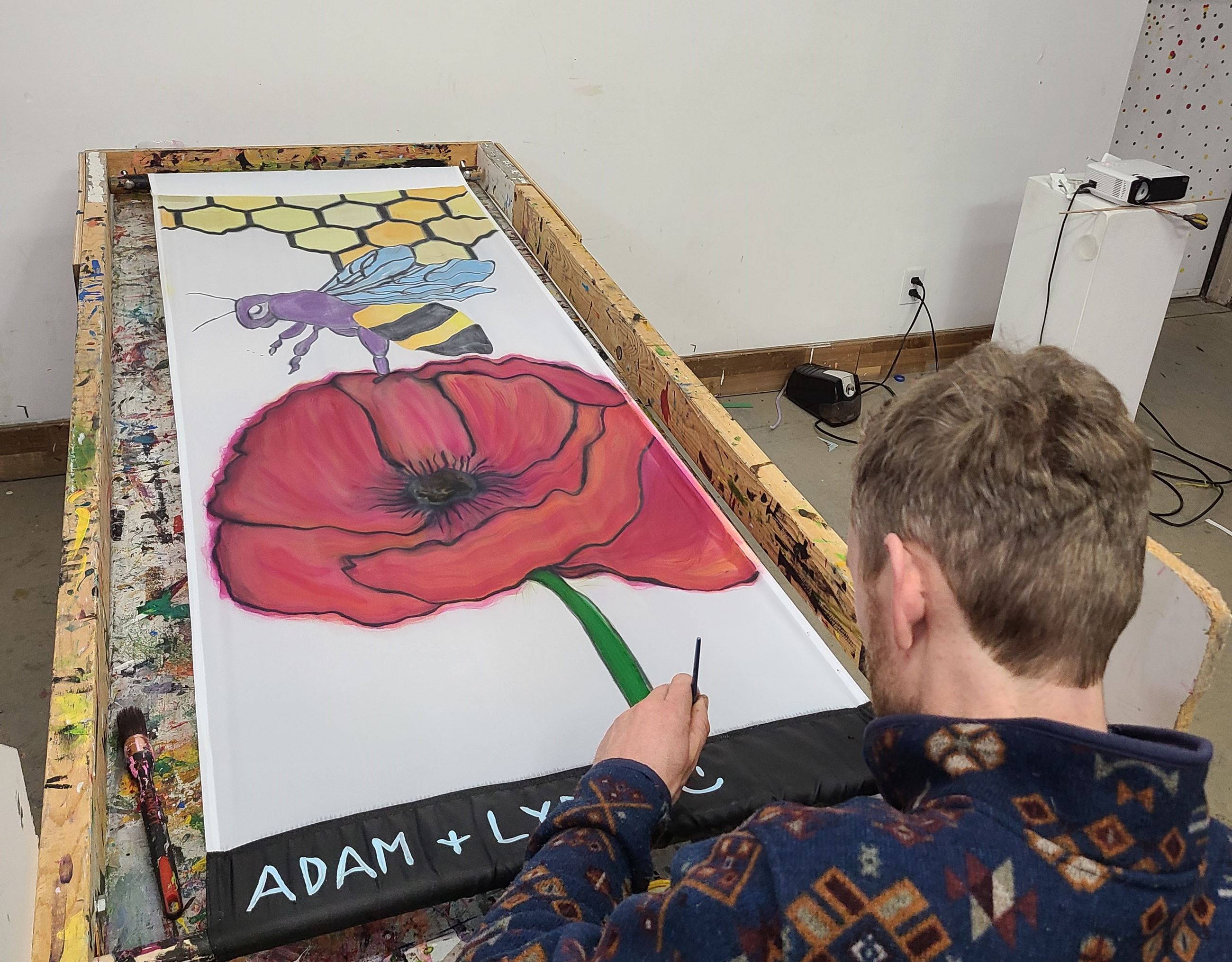 Man Painting a Banner Depicting a Bee on a Red Flower for the 2024 Art Banner Program